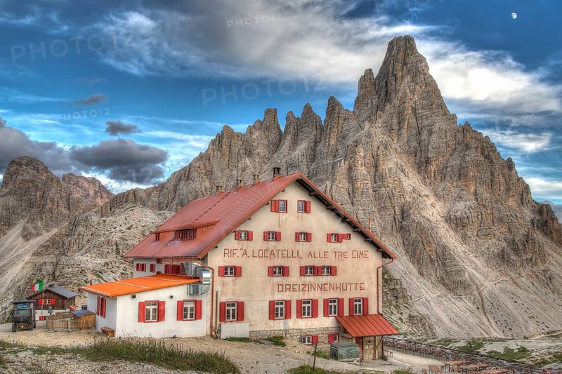 Mountain hut Dreizinnenhuette with rock massif Paternkofel in the evening, moon behind