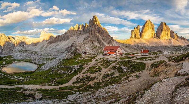 View of mountain hut Dreizinnenhuette and chapel with mountain lake rock massif Paternkofel and mountains three peaks in the sunset, panorama