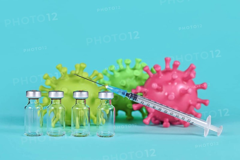 4 vaccine vials with syringes and corona virus models in background,