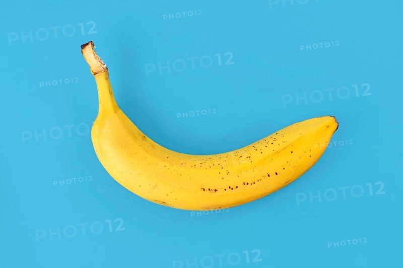 Single ripe banana with peel on blue background,