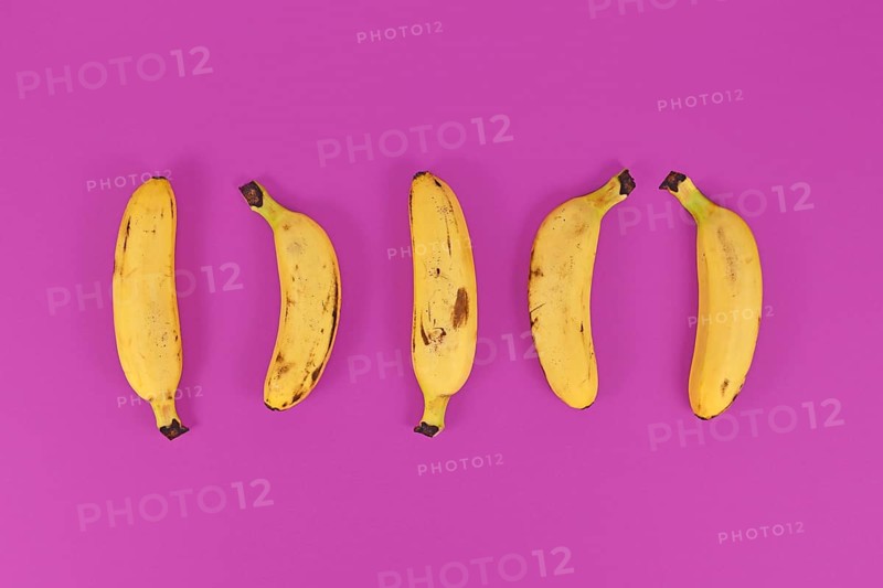 Five small snack bananas in a row on bright purple background,