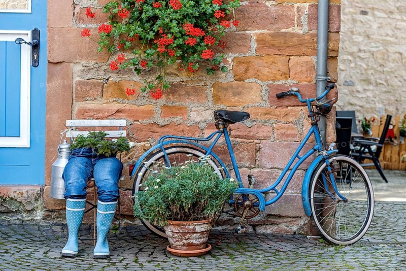 Curious decoration on a front door, blue jeans trousers in rubber boots with flower pot