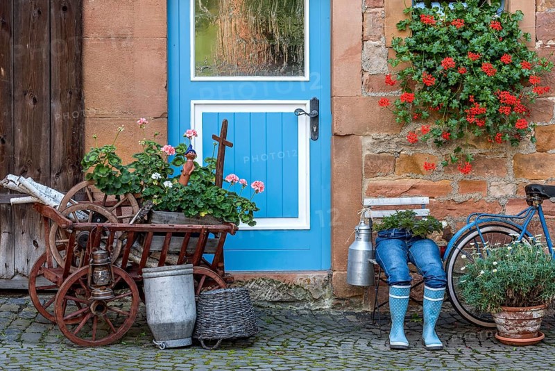 Curious decoration on a front door, blue jeans trousers in rubber boots with flower pot