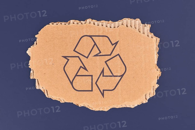 Piece of cardboard with recycling arrow sign on dark blue background,