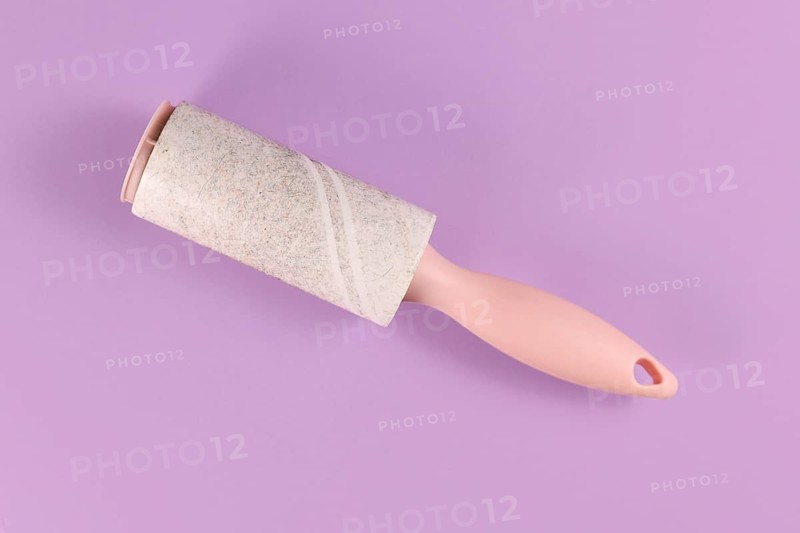Used fluff roller for cleaning clothes on violet background,