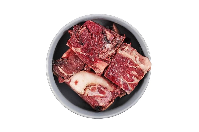 Dog bowl with big red chunks of meat with fat used for raw biologically appropriate feeding on white background,