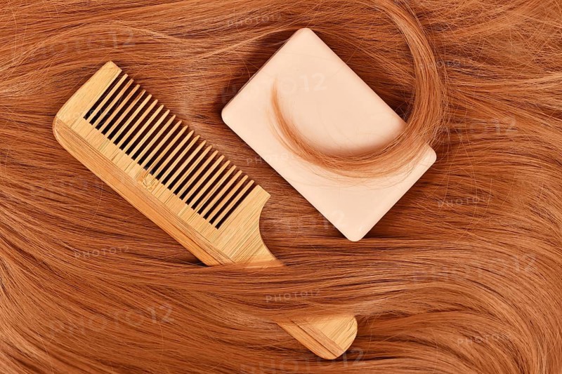 Solid shampoo bar and wooden comb on red hair. Concept for eco friendly healthy hair care routine,