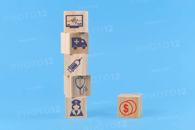 Concept for discrepancy between costs for medical treatments and funding depicted with wooden blocks with medical icons like nurse and ambulance and dollar sign,