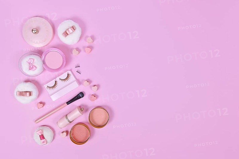 Pink makeup beauty products like brushes, powder or lipstick on side of pastel pink background with empty copy space