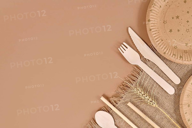 Eco friendly paper party plates and wooden cutlery in corner of beige background with copy space,