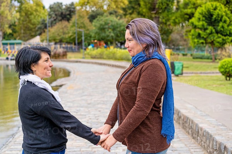 Lesbian couple in a park holding hands looking at each other,