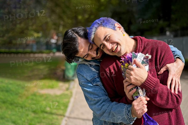 Couple of Latino gay men in a park embracing each other. One surprising the other with a bouquet of flowers as a gift,