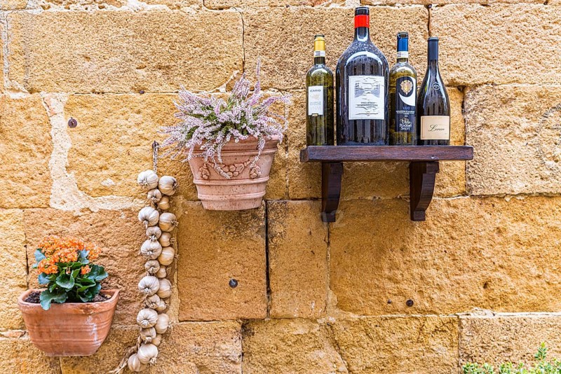 Wine bottles, flower box and garlic as decoration on a house wall in the centre of Pienza