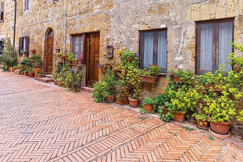 Old stone houses decorated with flower pots, diagonally laid brick pavement