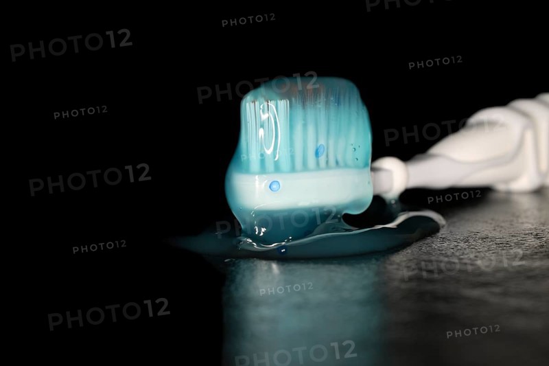Electric toothbrush with a blue transparent toothpaste, studio photography with black background