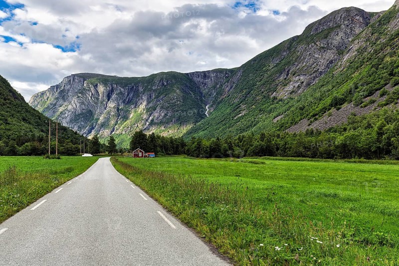 Single-lane country road through valley, typical landscape with high mountains