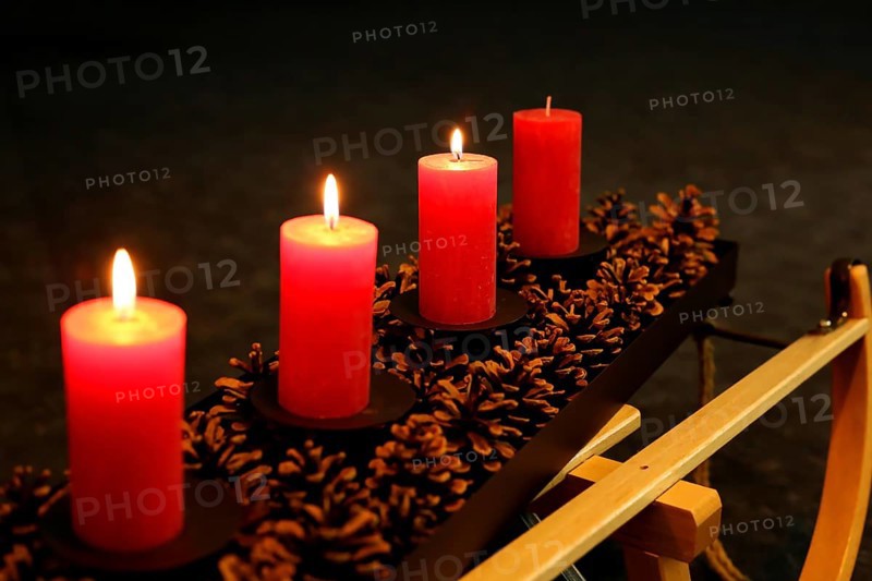 Four Advent candles decorated with pine cones on a sleigh, Third Advent three candles burning