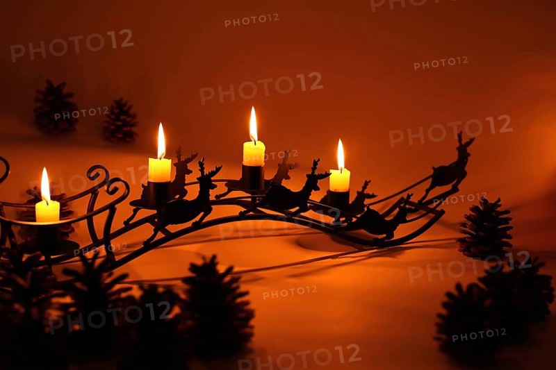 Fourth Advent with four lit candles on a sleigh with reindeer in diffuse red light,