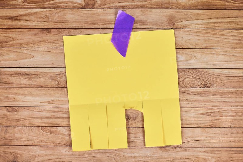 Yellow empty tear-off stub paper note without text on wooden wall,