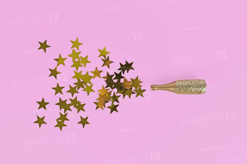 Golden star confetti splashing out of Champagne bottle on pink background,