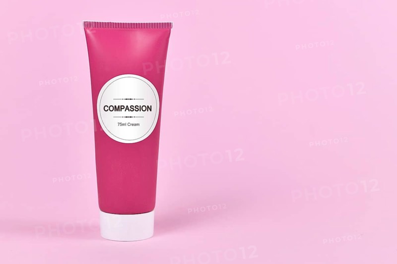 Compassion concept with cream tube with made up label saying Compassion, 75ml cream on pink background with blank copy space