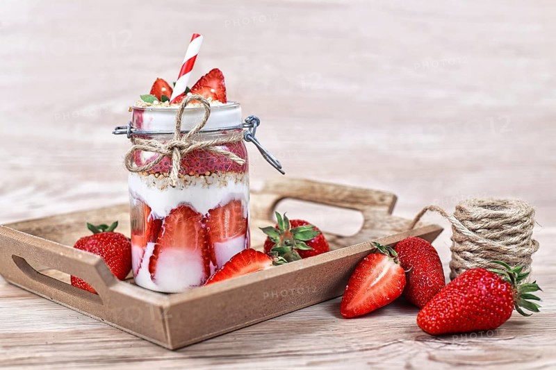 Strawberry fruit dessert with low fat yogurt, chia seeds and puffed quinoa grains layered in jar surrounded by berries on wooden background