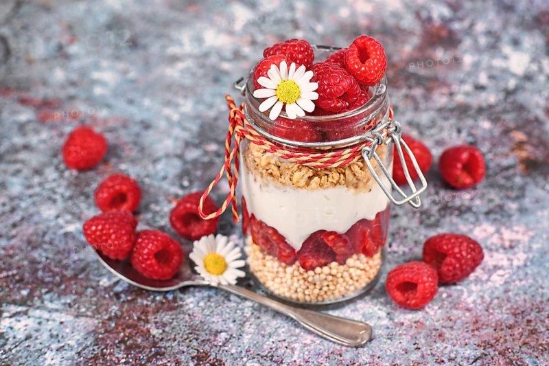 Healthy raspberry fruit dessert with skyr yogurt, granola and puffed quinoa grains layered in jar surrounded by ingredients