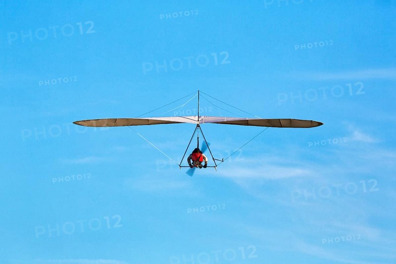 Motorised hang glider flying in slightly cloudy sky, text free space