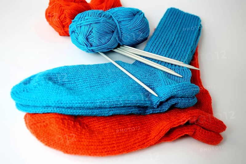 Self-knitted socks made of wool isolated against a white background in orange and blue with knitting needle and ball of wool,