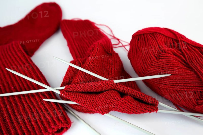 Self-knitted red socks made of wool isolated against a white background with knitting needle and ball of wool,