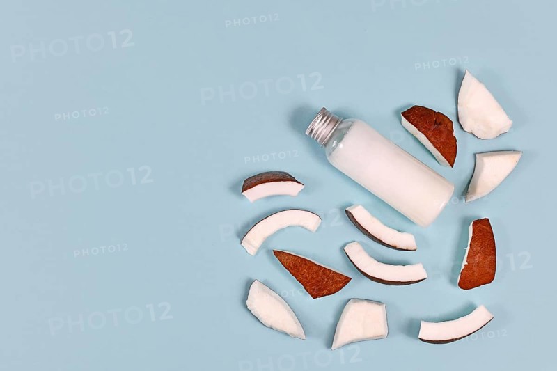 Slices of coconut fruit and bottle filled with coconut oil used for food preparation and cosmetic beauty products on blue background with copy space,