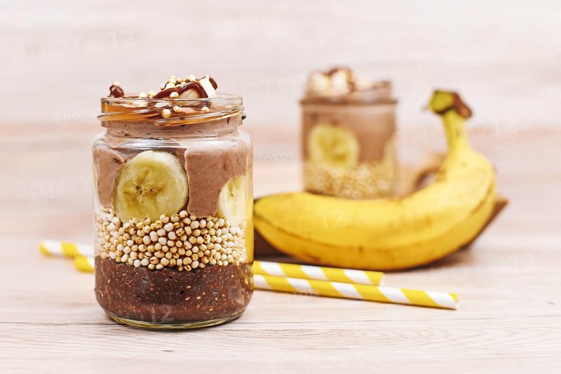 Layered healthy dessert with banana fruit slices, puffed quinoa grain and chocolate chia seed pudding in jar