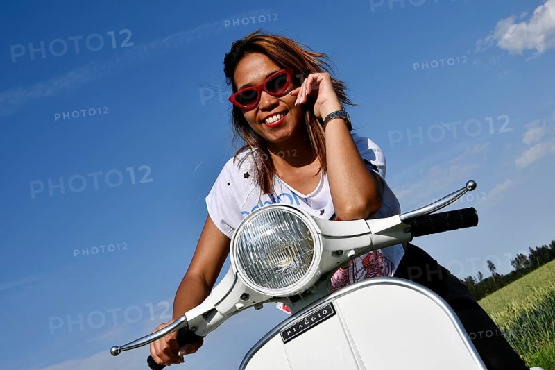 Woman with sunglasses sits on Vespa, rides on Vespa