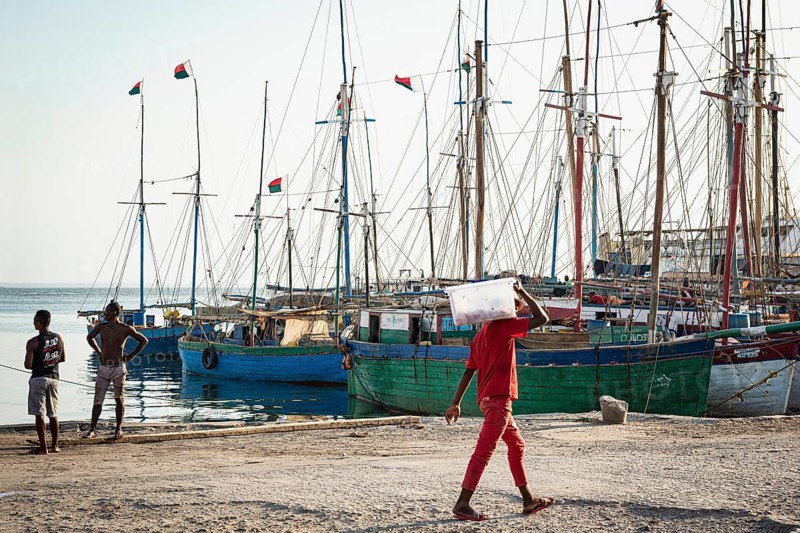Man in red clothes carrying sack, fishing boats behind