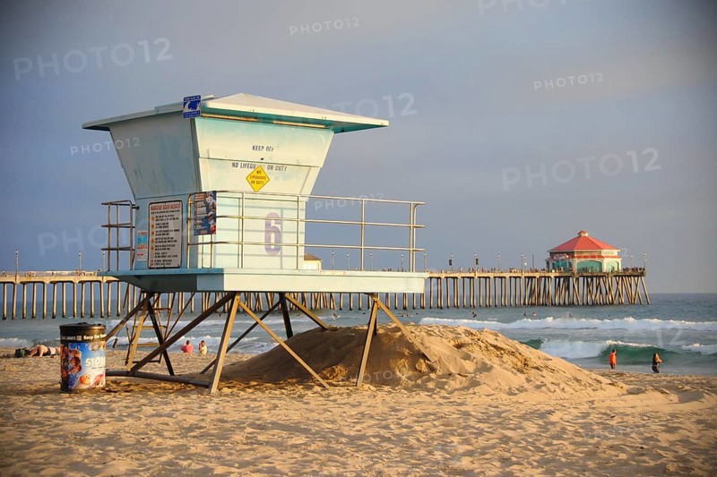 A lifeguard tower on a californian beach at sunset. Far behind is Huntington Beach Pier,
