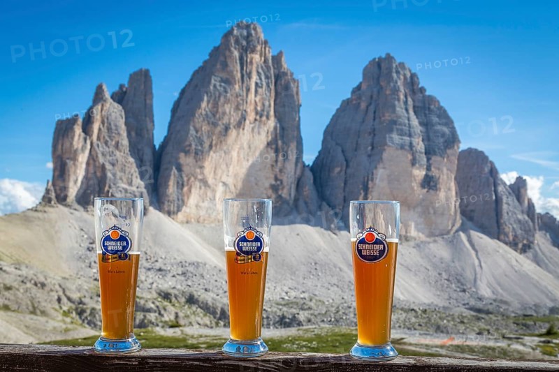 Three wheat beer glasses with wheat beer in front of the Drei Zinnen mountain range, north faces