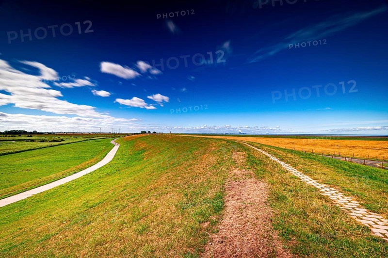 View from the dike in Greetsiel towards Pilsum in the Pilsum lighthouse in summer with scattered clouds