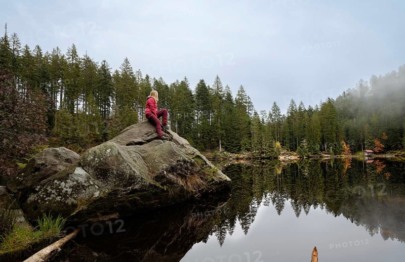 Woman in red on rocks in Glaswaldsee surrounded by forest