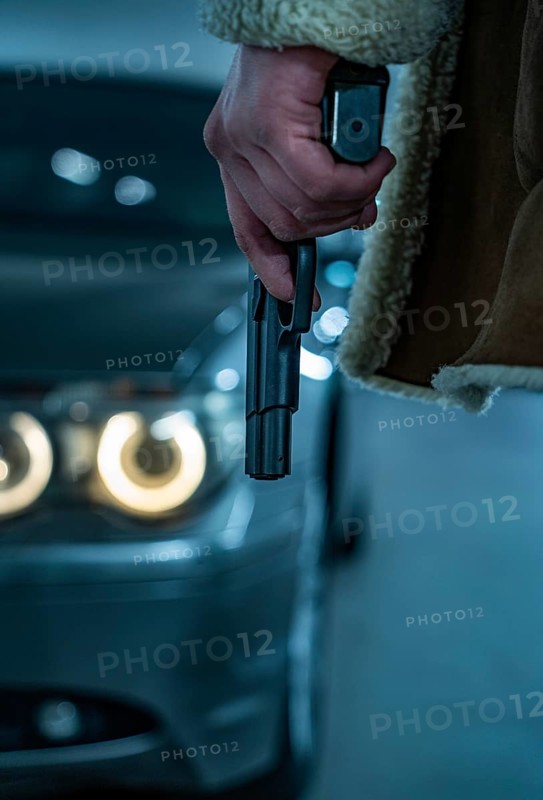 Criminal man with gun in hand in front of 7 series BMW underground