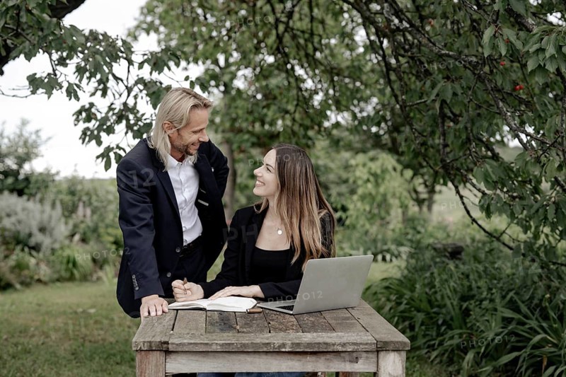 Businessman and businesswoman working in the open on a laptop at a wooden table
