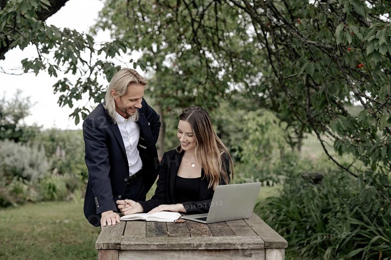 Businessman and businesswoman working in the open on a laptop at a wooden table