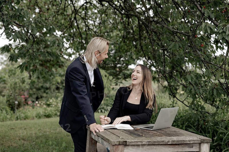 Businessman and businesswoman working in the open on a laptop at a wooden table