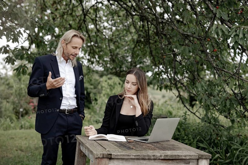 Businessman and businesswoman working in the open on a laptop at a wooden table