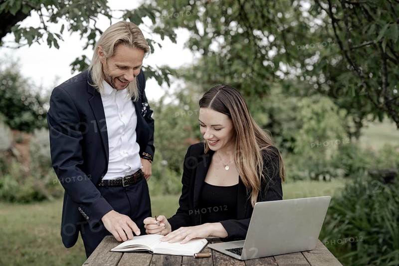 Businessman and businesswoman working in the open on a laptop at a wooden table