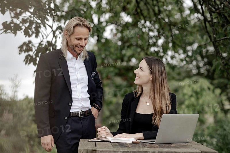 Businessman and businesswoman working in the open on a laptop at a wooden table