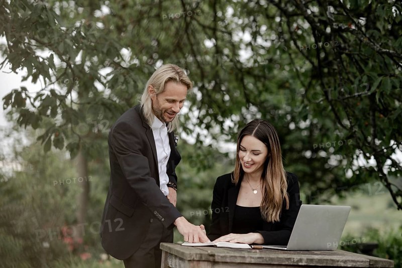 Businessman and businesswoman working in the open on a laptop at a wooden table
