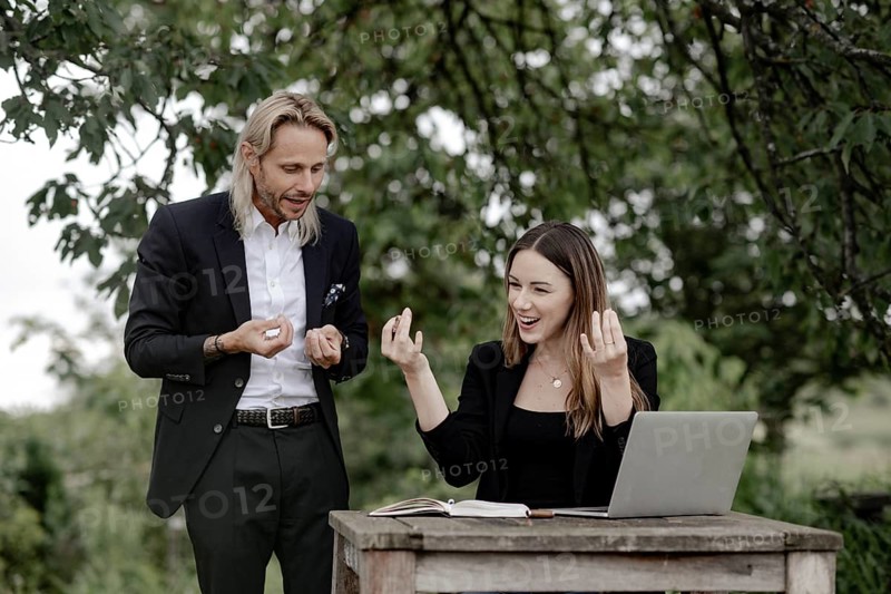 Businessman and businesswoman working in the open on a laptop at a wooden table