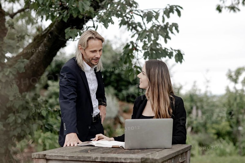 Businessman and businesswoman working in the open on a laptop at a wooden table