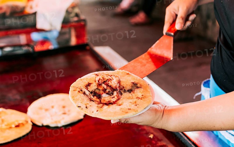 Hand holding a freshly made pupusa on a plate