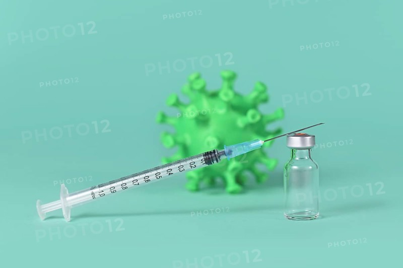 Vaccine vial with syringe and corona virus model in background